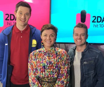 Three radio hosts smiling in front of 2DayFM branding on screens.