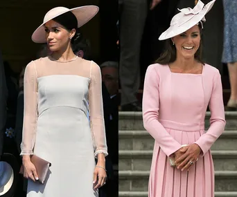 Two women wearing elegant pastel dresses and hats at a formal event, standing and smiling.