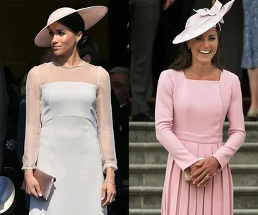 Two women wearing elegant pastel dresses and hats at a formal event, standing and smiling.
