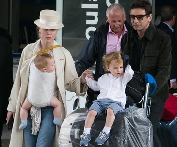 Family traveling with luggage and two children; one baby in a carrier, another child on a luggage cart.