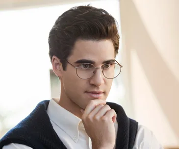 "Person wearing glasses and white shirt, hand on chin, looking thoughtful in soft lighting."