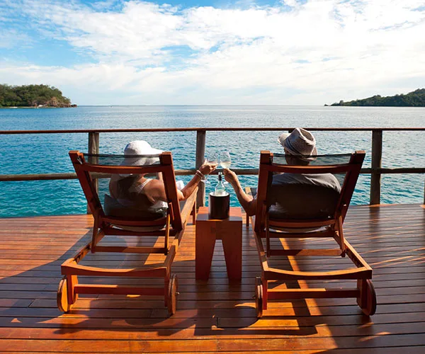 Couple toasting on deck chairs overlooking the ocean in Fiji.