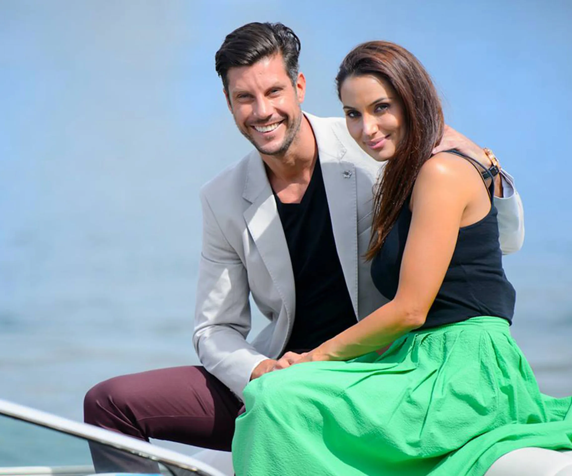 A smiling couple sitting together on a boat with a calm water backdrop.