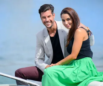 A smiling couple sitting together on a boat with a calm water backdrop.