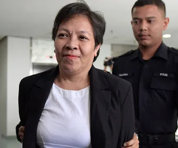 A woman in a white shirt and black blazer escorted by a police officer.