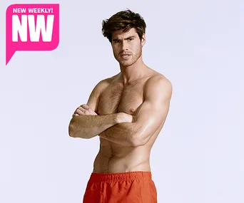 Shirtless man in red shorts with arms crossed, posing confidently; NW magazine logo in corner.