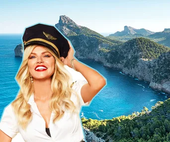 Blonde woman in pilot hat smiling with scenic coastal cliffs and blue sea in the background.