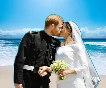 A couple in wedding attire kissing on a beach under a clear blue sky.