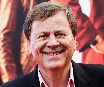 "Smiling man in a suit at an event, red background."