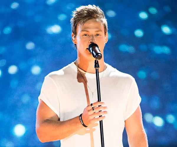 Singer in white T-shirt performing on stage with a microphone, blue bokeh background.