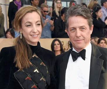 Two people in formal attire posing at an event, with others in the background taking photos.