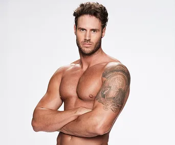 Muscular man with a tattooed arm posing shirtless against a white background.