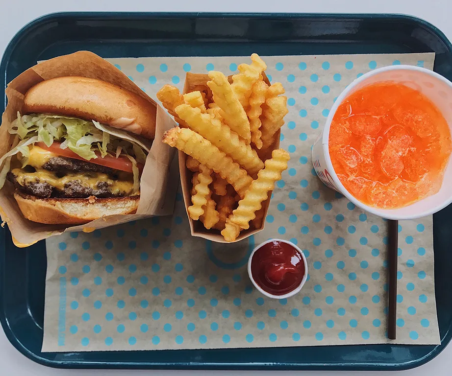 Burger, crinkle-cut fries with ketchup, and orange soda on a blue tray with polka dot paper.