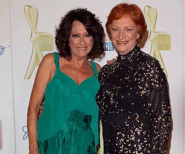 Two women posing at a TV event, one in a green dress and the other in a black sequined outfit.