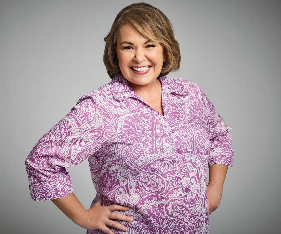 Person smiling in a pink paisley-patterned blouse against a gray background.
