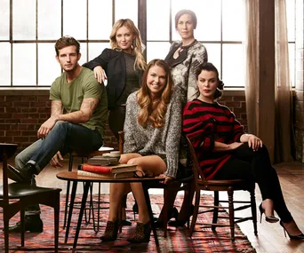 Group photo of five individuals in a stylish room with large windows and a red-patterned rug, exuding a casual yet chic vibe.