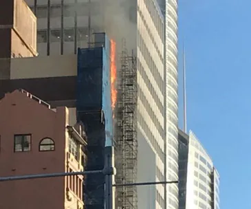 "Fire on a high-rise building in Sydney, with flames and smoke visible from scaffolding."