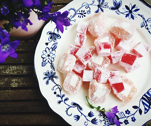 Plate of assorted Turkish delight on a floral-patterned dish with purple flowers beside.