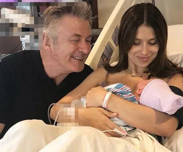 Man and woman in hospital bed holding newborn baby, smiling.