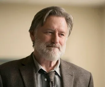 Man with gray hair and beard in a suit, smiling softly; scene from "The Sinner" season 2.