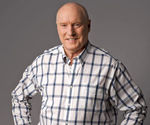 Man in a checkered shirt smiles against a gray background.