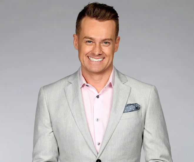 Man in a light gray suit and pink shirt smiling at the camera.