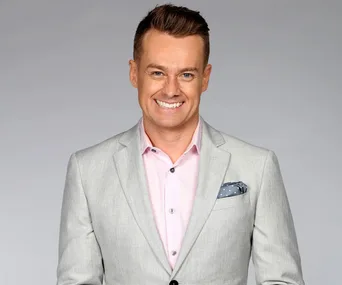 Man in a light gray suit and pink shirt smiling at the camera.