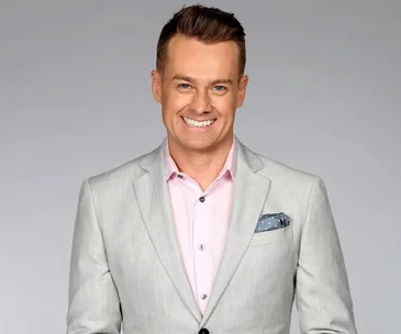 Man in a light gray suit and pink shirt smiling at the camera.