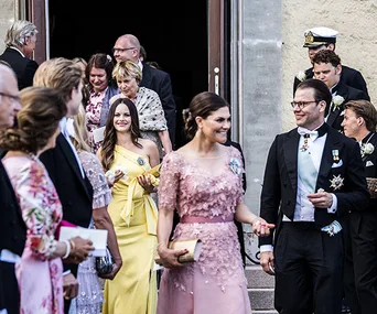 Royal guests leaving a wedding venue, including people in formal attire and uniforms, smiling and interacting.