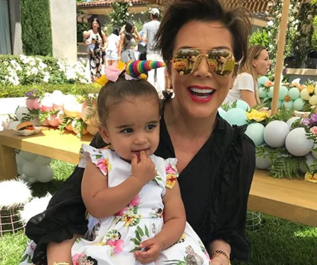 A woman in sunglasses and a child with a unicorn horn headband at an outdoor party with colorful decor.