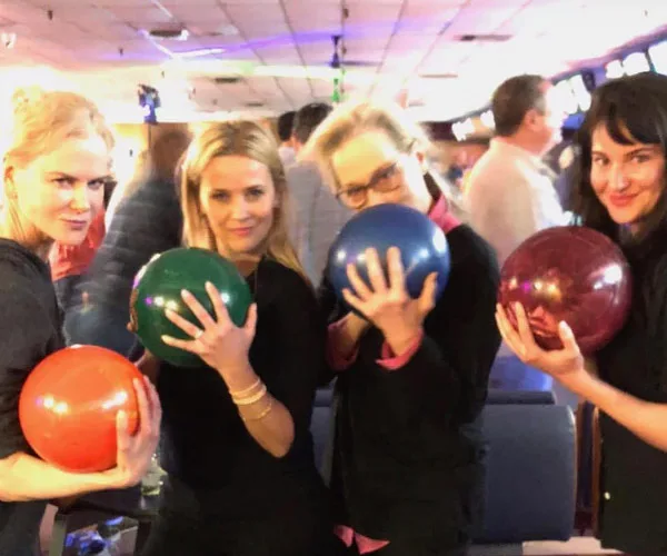 Group of women holding bowling balls, smiling, in a bowling alley setting.