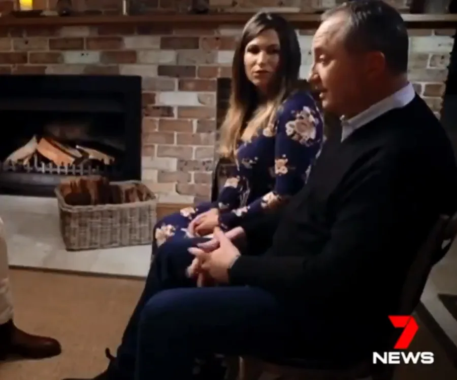 Interview setting with two people seated beside a fireplace, logo of 7 NEWS at the bottom right.