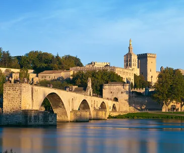 Stone bridge and Papal Palace in Avignon, France, under a clear blue sky.