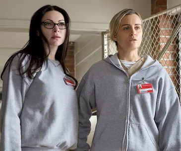 Two women in prison uniforms stand side by side, looking serious.