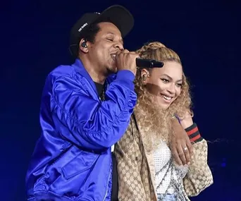 Two performers on stage; one singing with a microphone, the other smiling with an arm around them.