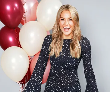 Smiling woman in a polka dot dress with colorful balloons, Logie Awards 2018 nominees event backdrop.