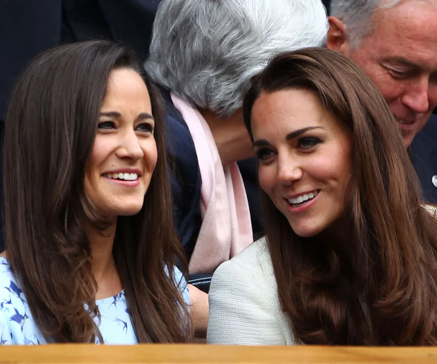 Two women smiling, sitting together in a crowded outdoor setting.