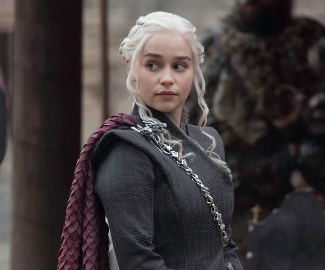 Daenerys Targaryen in a dark outfit with a braided cape, looking to the side in Game of Thrones.