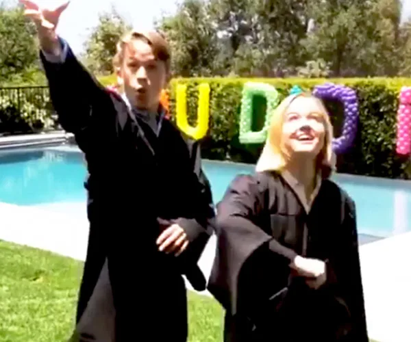 Graduates in robes celebrate by a pool with colorful "You Did It" balloons in the background.