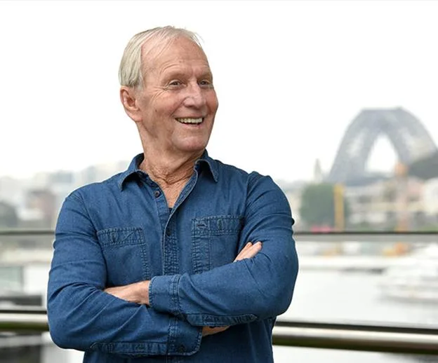 Man in a blue shirt smiling with Sydney Harbour Bridge in the background.