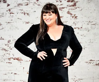 Woman in a black dress poses confidently against a white brick wall.