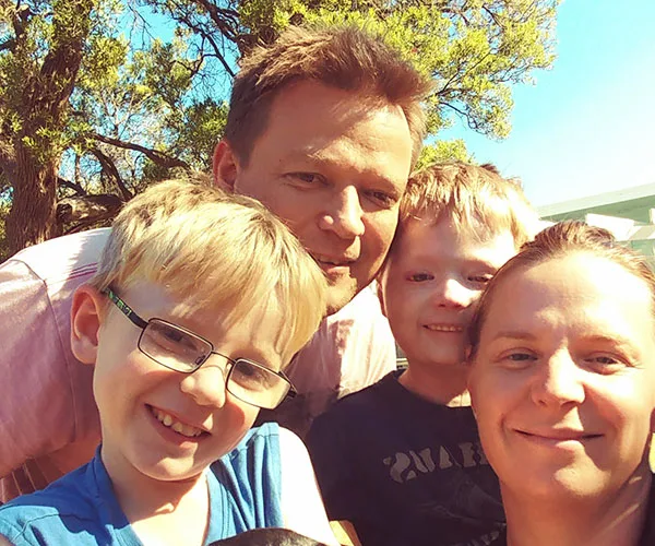 A smiling family outdoors under a tree with clear blue sky.