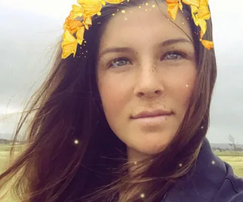 A woman with long hair wearing a digital golden leaf crown in an outdoor setting.