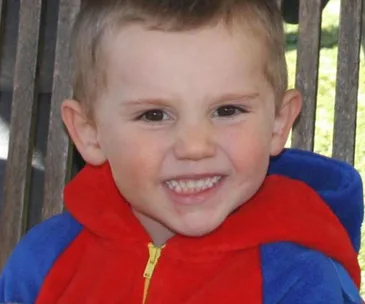 A young child smiling, wearing a red and blue hoodie.