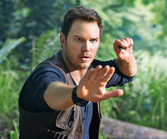 Character Owen Grady from "Jurassic World" raises hands defensively in a jungle setting.