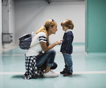 A mother crouches and talks to her young son in a parking garage, emphasizing a point with her finger.