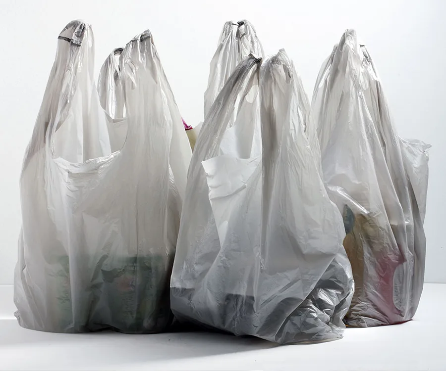 Plastic shopping bags filled with various items, standing upright against a plain background.