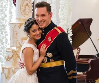 A couple in wedding attire smiles warmly, standing close together in front of a floral-decorated pillar indoors.
