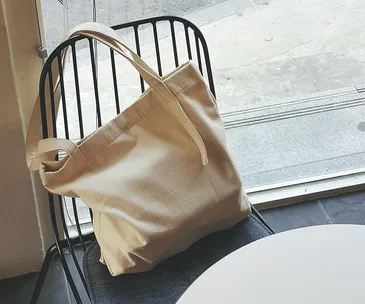 Reusable beige shopping bag on black metal chair near window.
