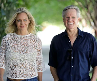 A woman in a lace top and a man in a dark shirt smiling while walking outdoors.
